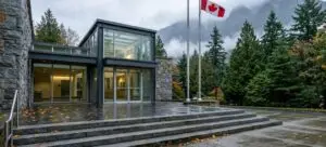 Entrance and stone steps of a modern provincial courthouse in British Columbia on an overcast autumn day, with a Canadian flag and mountains behind